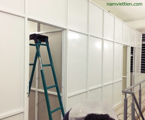 Vách ngăn nhôm kính khung trắng đang lắp đặt, thợ đứng trên thang nhôm